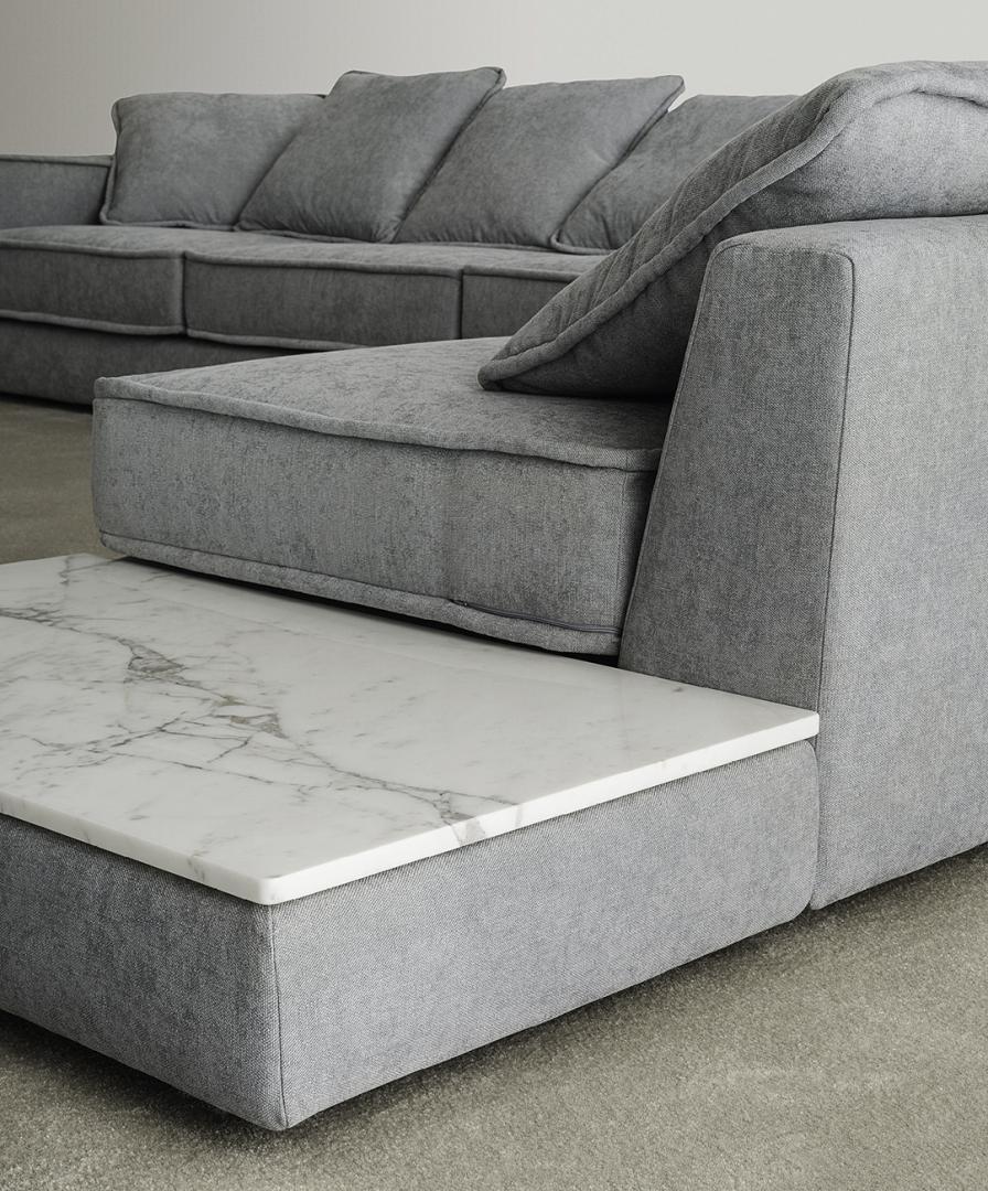 Close-up of a gray sectional sofa with plush cushions and a built-in marble side table, perfect for modern living spaces