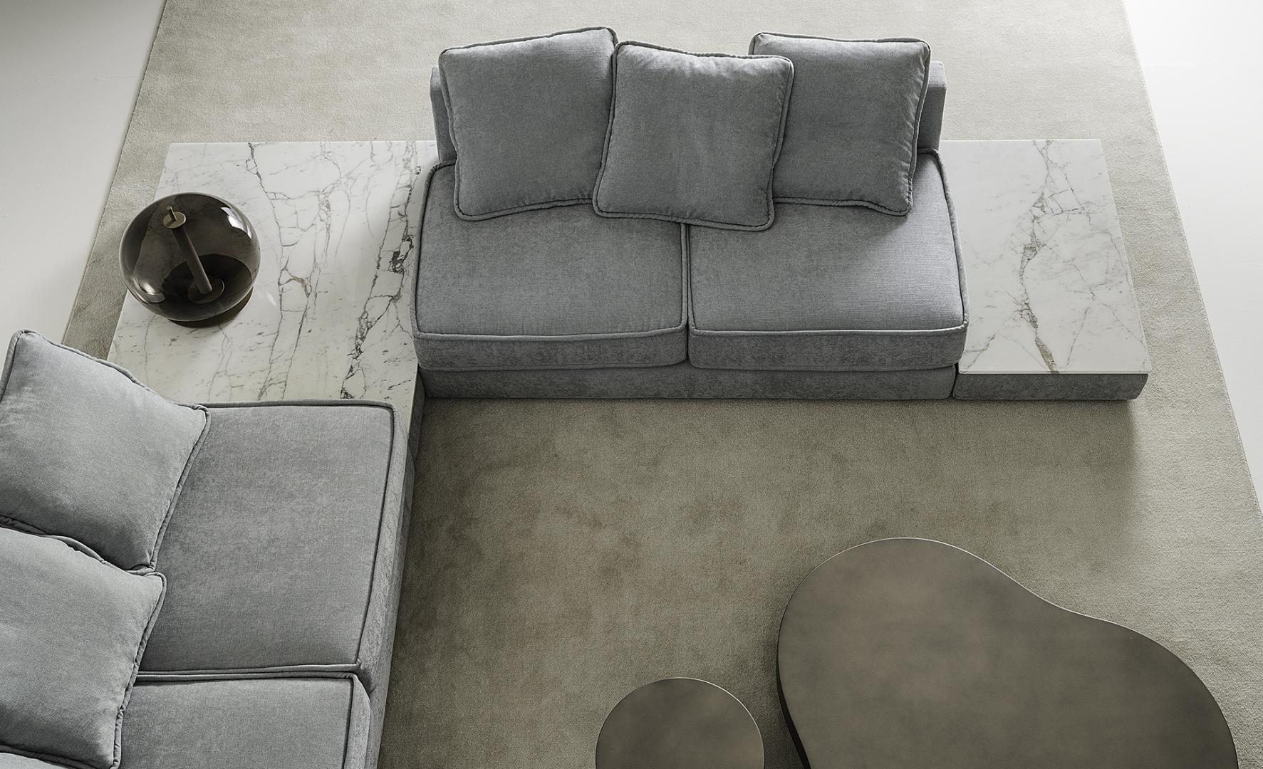 Overhead view of a modern living room featuring a gray modular sofa, marble side tables, and metal coffee tables on a neutral rug