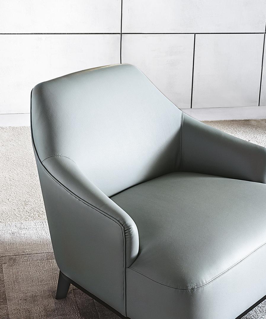 Close-up of the Casamilano Arne armchair in light gray leather. A modern accent chair with clean lines against a white tiled wall