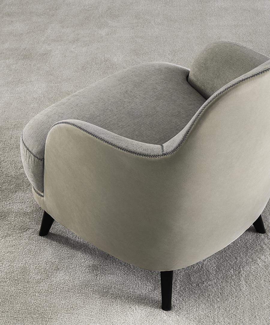 Close-up of the Casamilano Liz armchair featuring a light gray fabric seat, beige leather back, and black wooden legs on a gray carpet