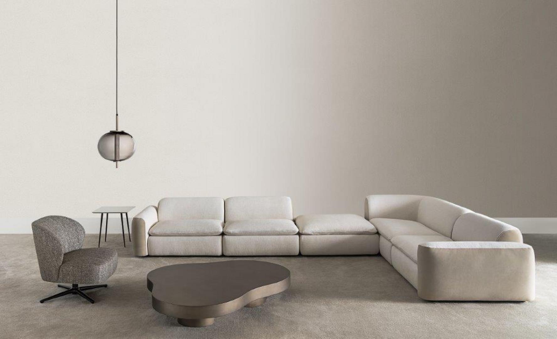 Modern living room featuring a Casamilano Dhora Slim armchair, modular sofa, metal coffee table, and pendant light. Neutral color palette, luxury furniture