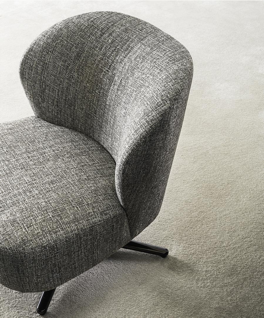Close-up of the Dhora Slim armchair by Casamilano, featuring gray upholstery, a curved back, and a swivel base, perfect for modern living spaces