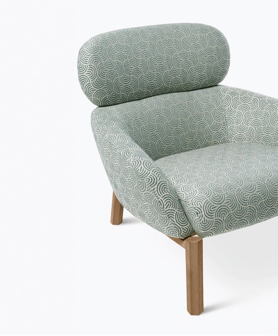Close-up of the Casamilano Elton armchair featuring patterned upholstery, wooden legs, and a headrest. Modern seating for stylish interior design