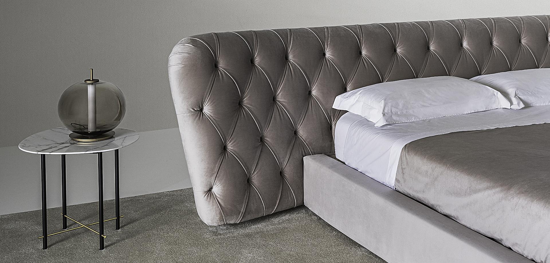 Close-up of a luxurious bedroom featuring the Casamilano Royale Capitonné bed with tufted headboard, marble nightstand, and glass lamp