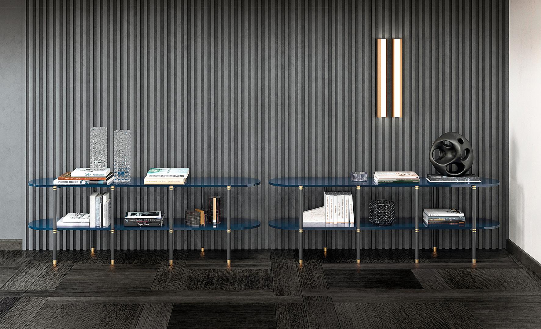 Interior with modern console tables featuring blue glass shelves, clear acrylic legs, gold accents, books, vases, and decorative objects against a striped wall
