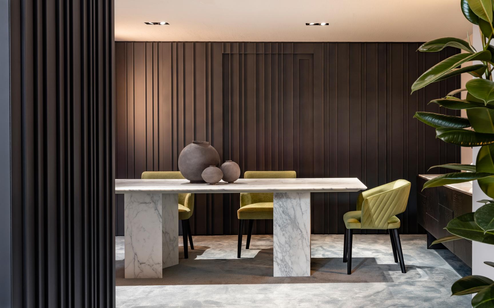 Modern dining room featuring a Carrara marble dining table and Quilted Comfort upholstered chairs against a dark paneled wall.