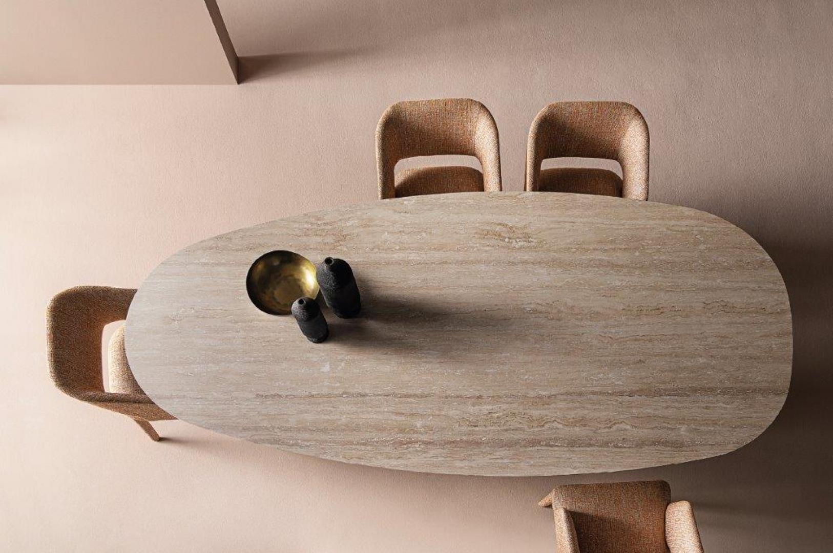 High-angle view of Casamilano Arne travertine dining table with upholstered chairs in a minimalist setting. Modern, luxury dining room furniture