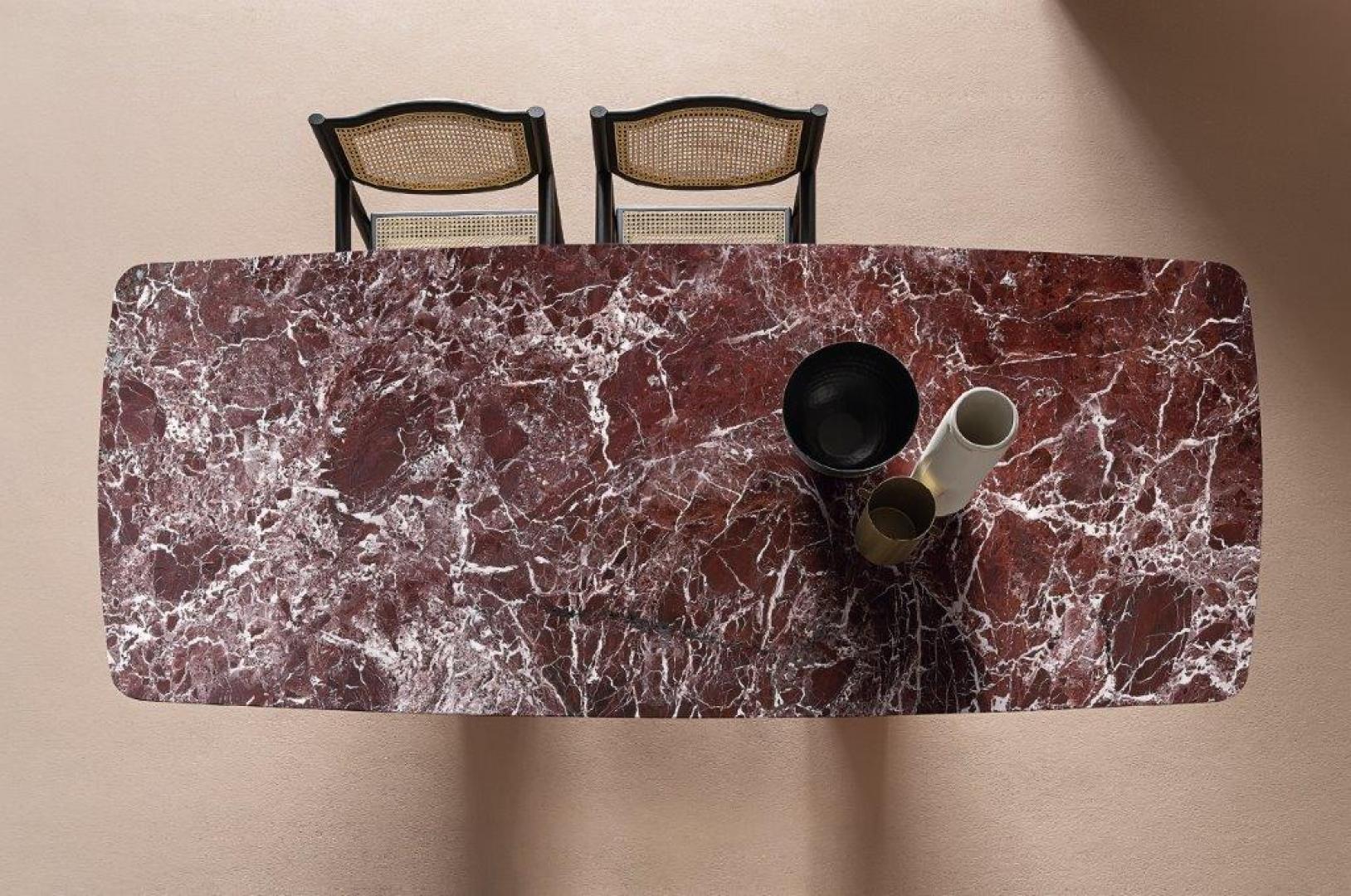 Overhead view of Casamilano Arne dining table with red marble top, paired with black-framed cane back chairs, vases, and bowl