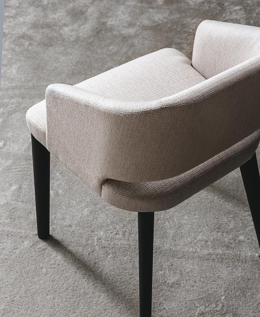 Close-up of the Elsa dining chair by Casamilano, a modern upholstered chair with black legs on a gray carpet, perfect for any space