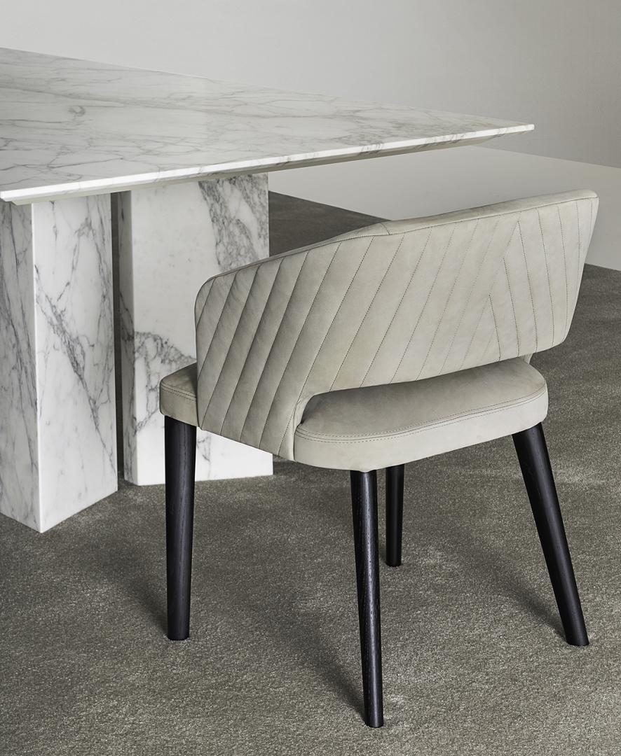 Quilted leather dining chair beside marble table on carpet.