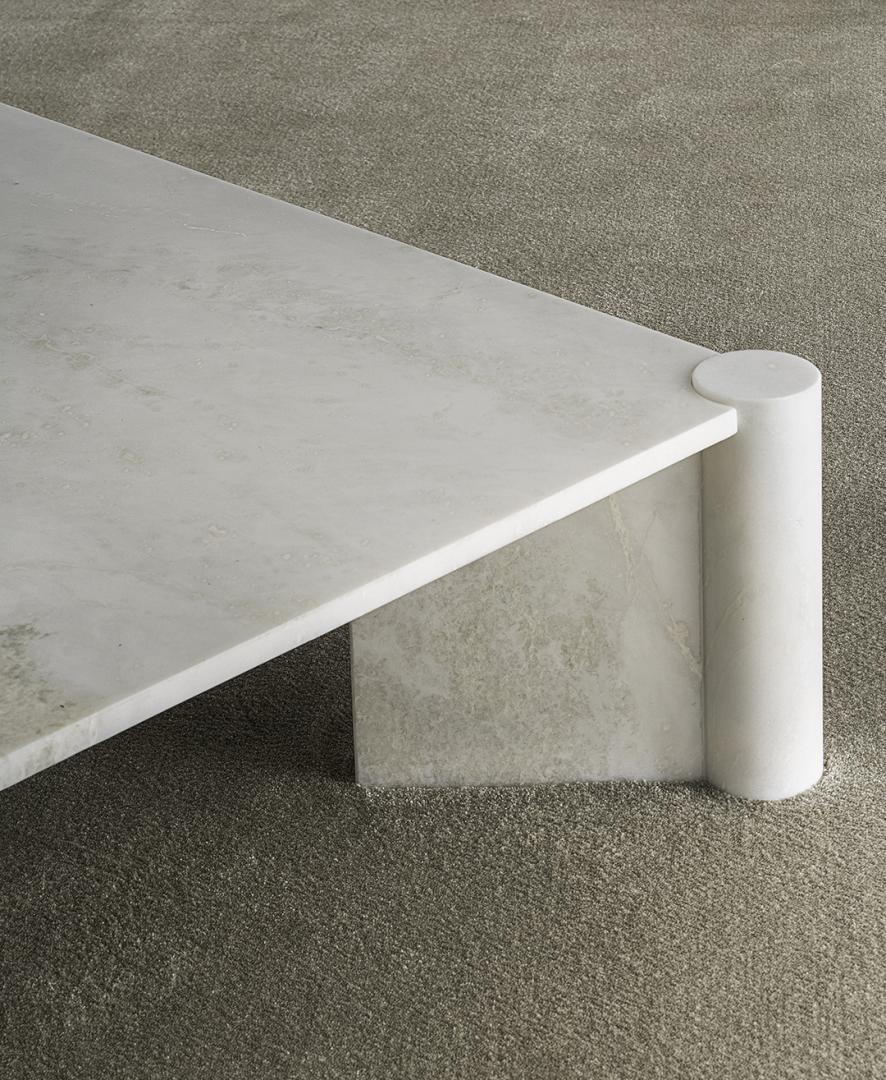 Close-up of Casamilano Petra coffee table: white marble top, cylindrical leg, gray rug. Modern, minimalist, luxury living room decor