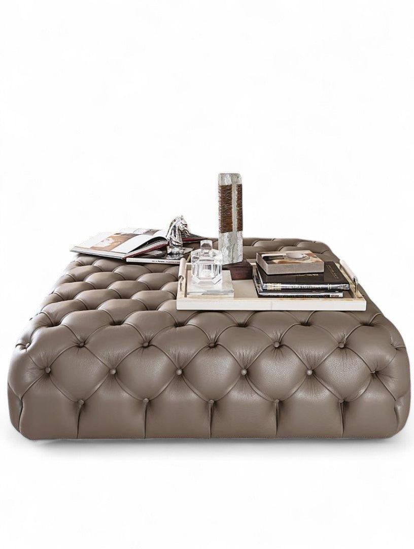 Tufted leather ottoman coffee table with decorative accessories on white background.