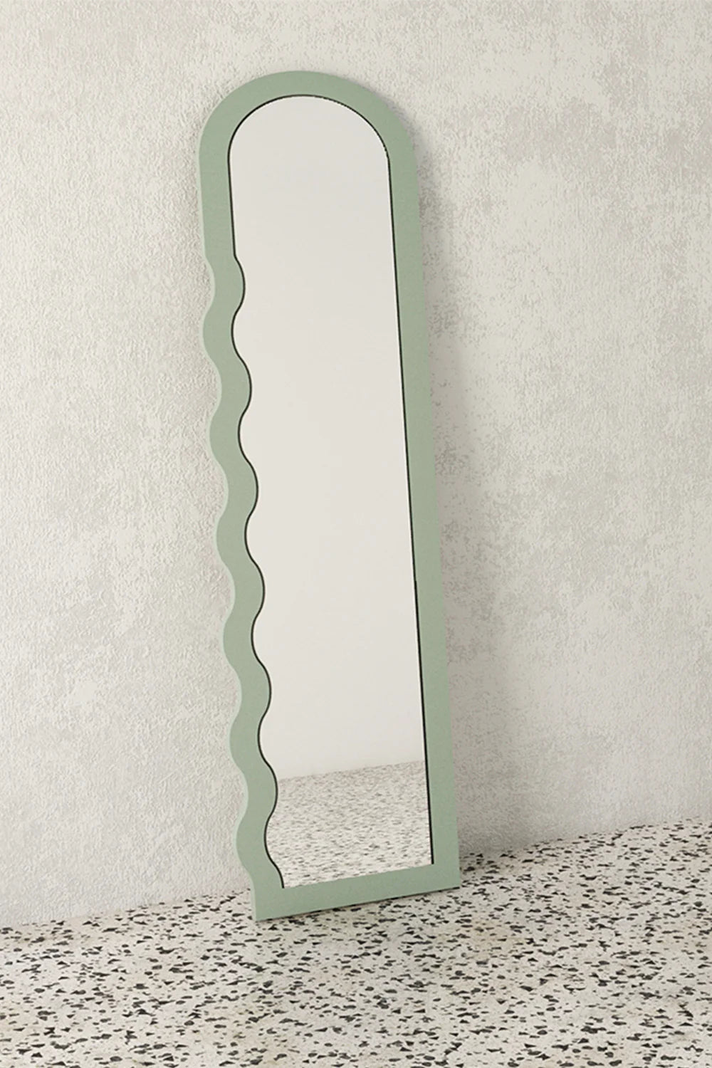 Full-length mirror with sage green wavy frame leaning on wall