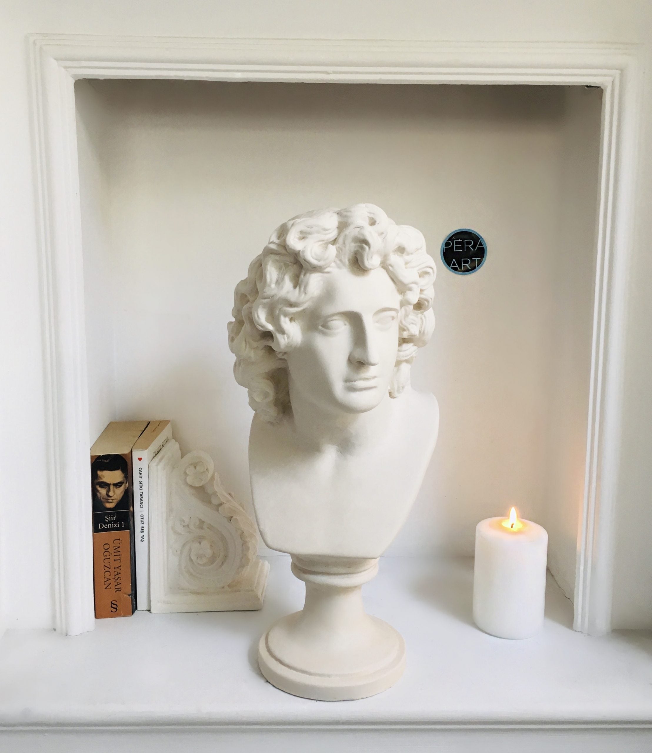 White plaster bust sculpture in niche with books and candle
