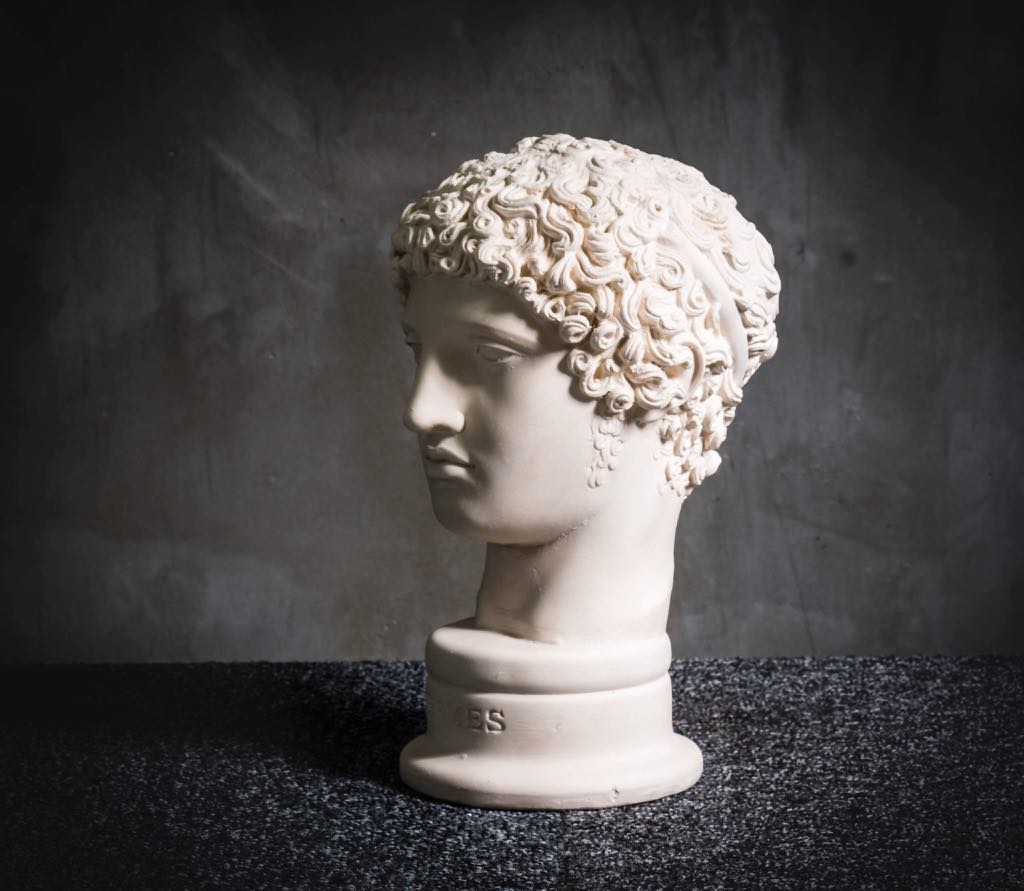White plaster head sculpture with curly hair on dark surface