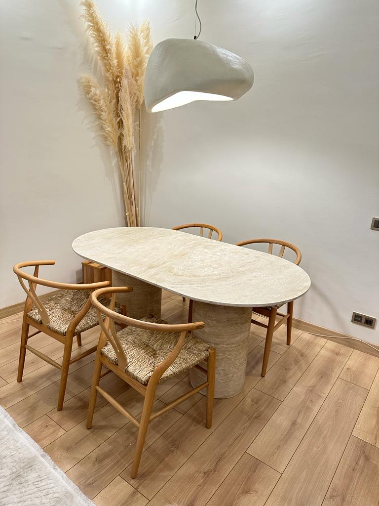 Interior of dining area featuring a Luzione travertine oval table, wishbone chairs, pendant light, and pampas grass creating a modern, inviting space