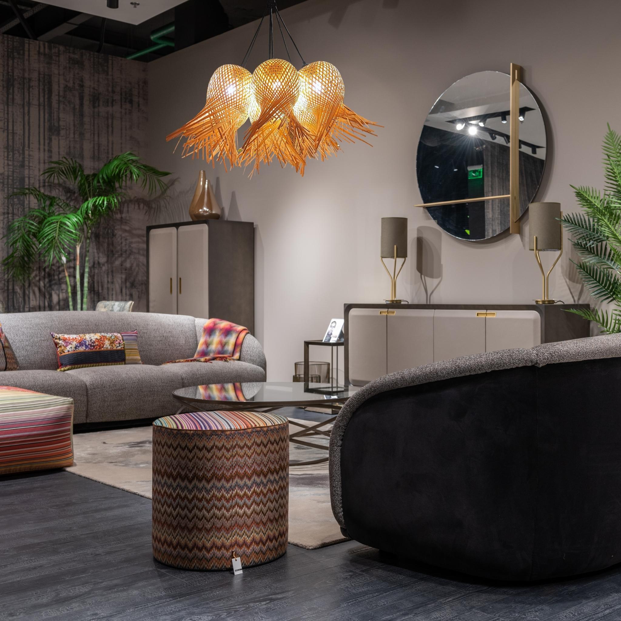 View of a living room with gray sofa, patterned ottomans, and rattan chandelier