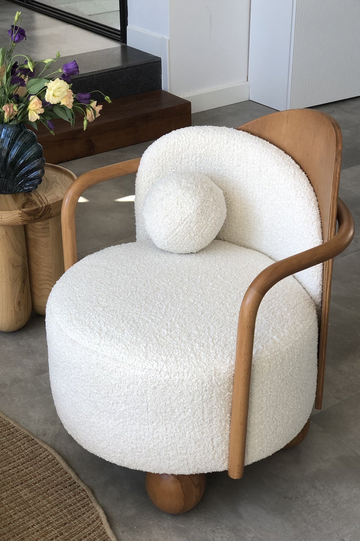 Interior view of white boucle armchair with wood frame and side table.