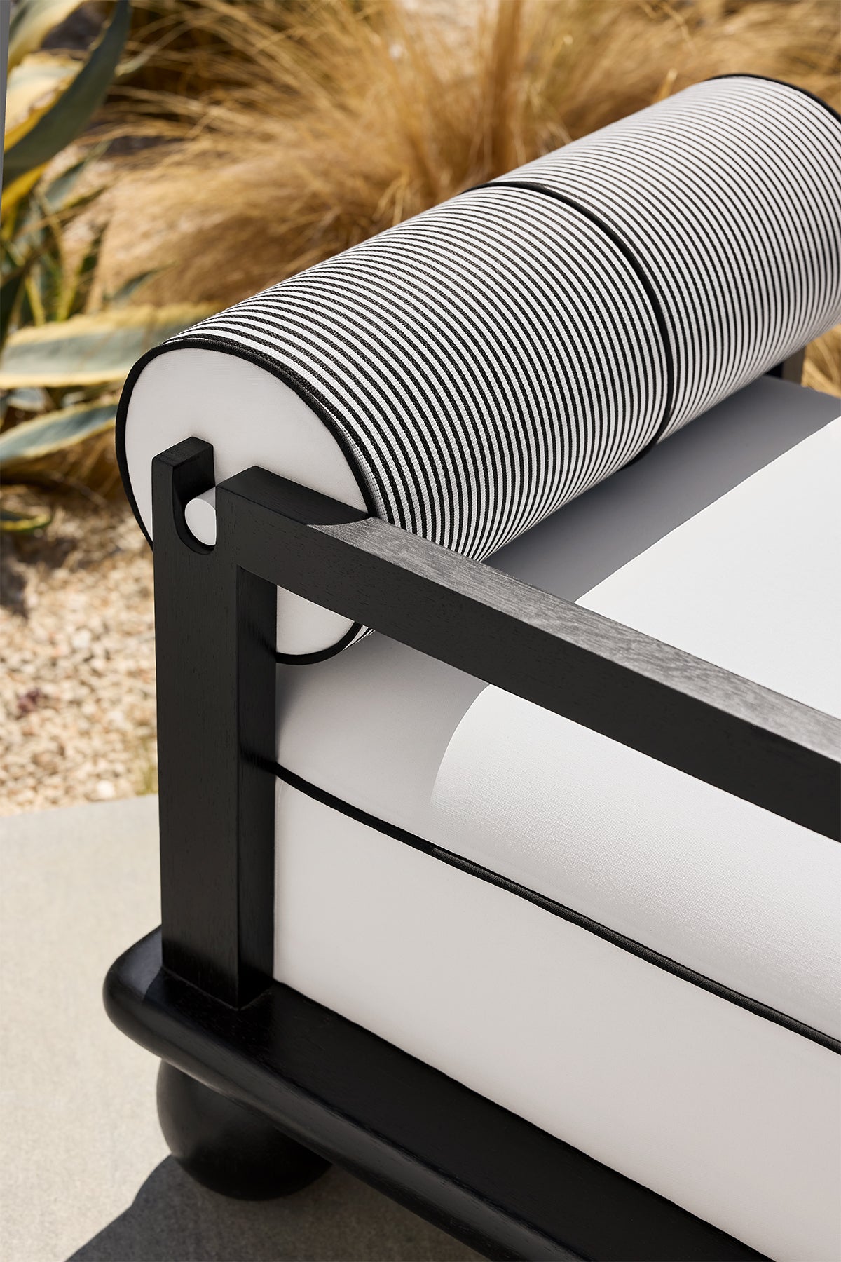 Close-up of a modern outdoor chair with a black wood frame and a white cushion with black and white stripes, headrest, and backrest.