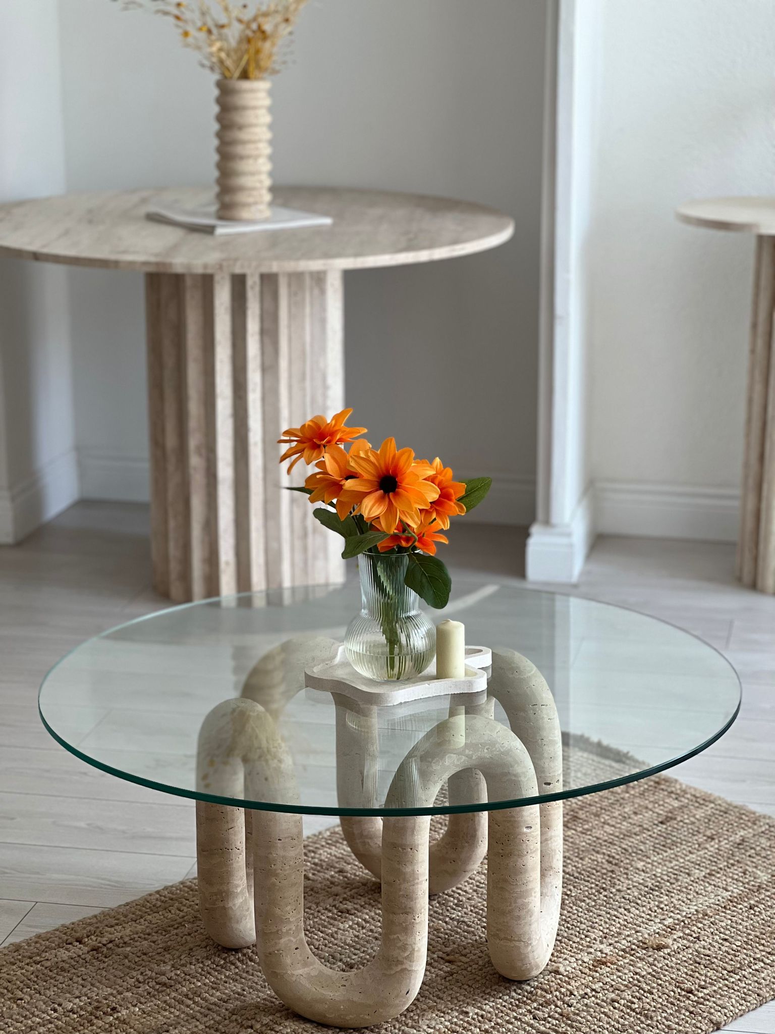 Luzione glass coffee table with travertine base, styled with orange flowers and candles in a modern living room with a jute rug