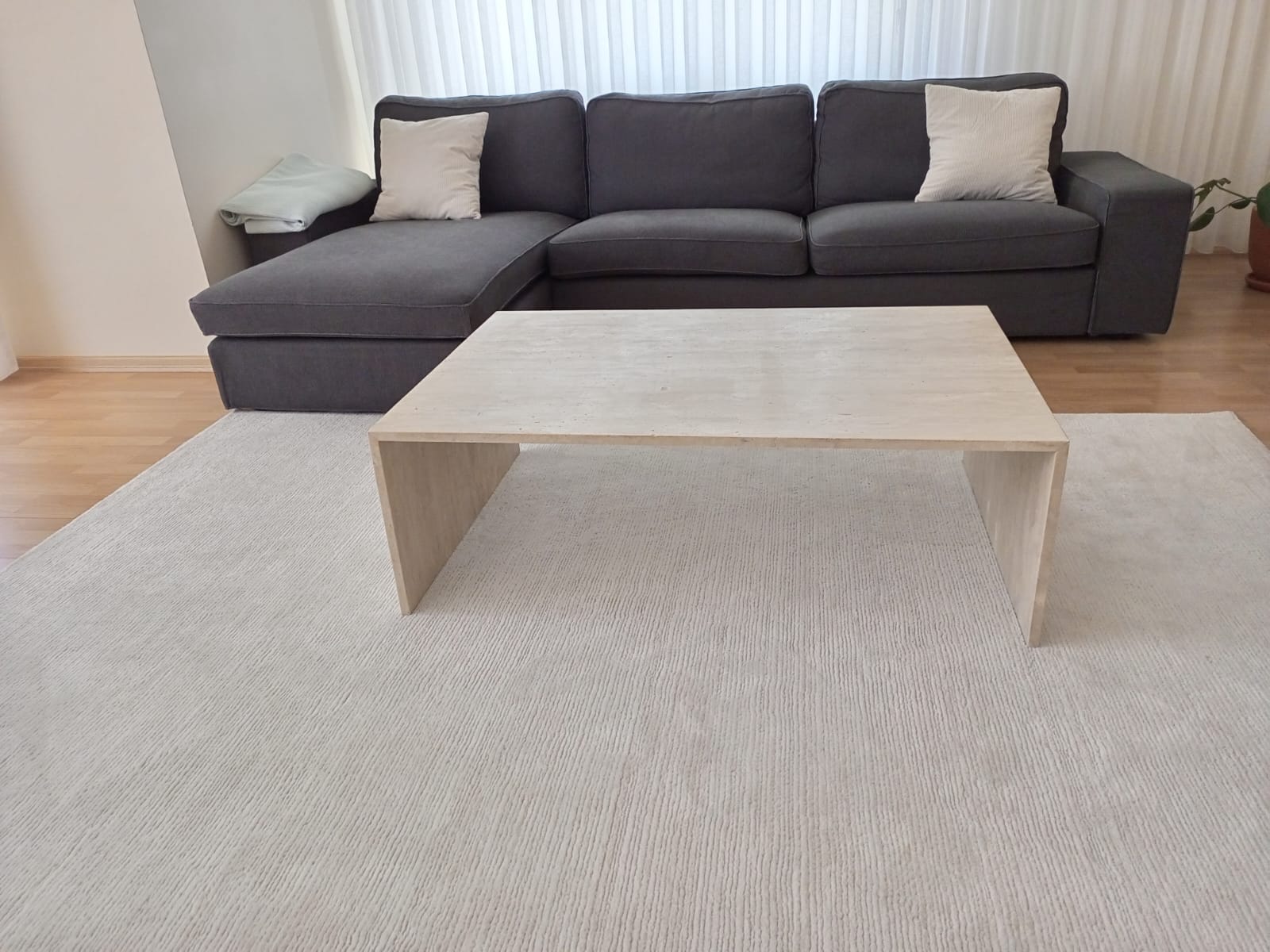Modern minimalist living room featuring a Luzione flat top C-shaped travertine coffee table, dark gray sofa, and textured cream rug