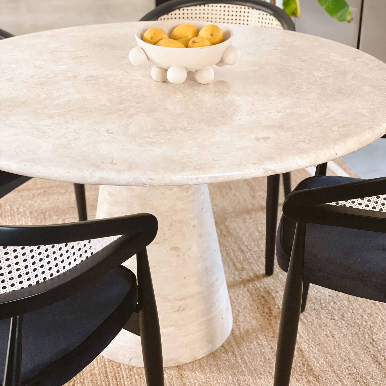 Luzione Round Travertine Dining Table with Funnel Leg and Black Cane Back Chairs. Modern dining room furniture for stylish homes.
