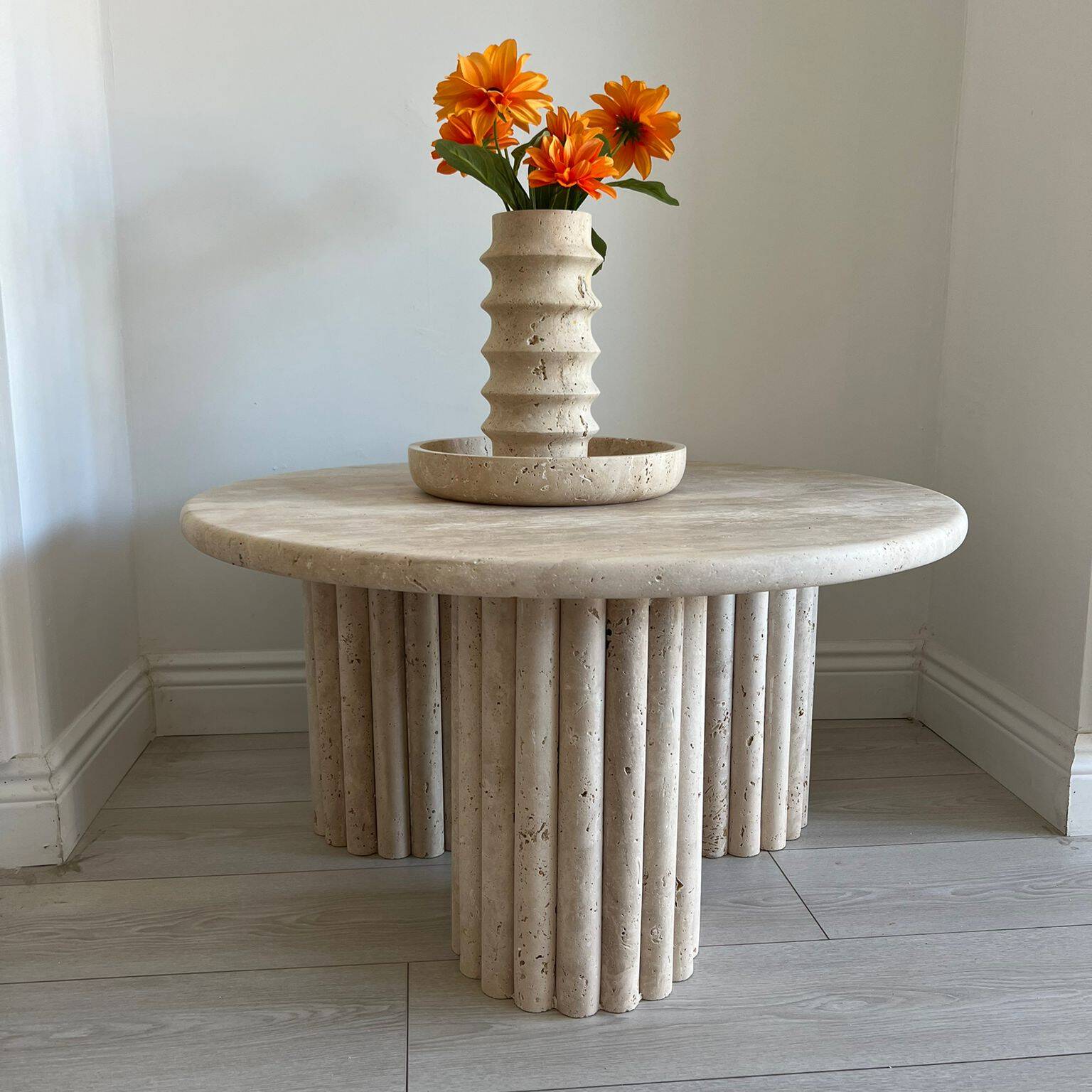 Eye-level view of a Luzione travertine coffee table with orange flowers in a matching vase, set in a modern living room