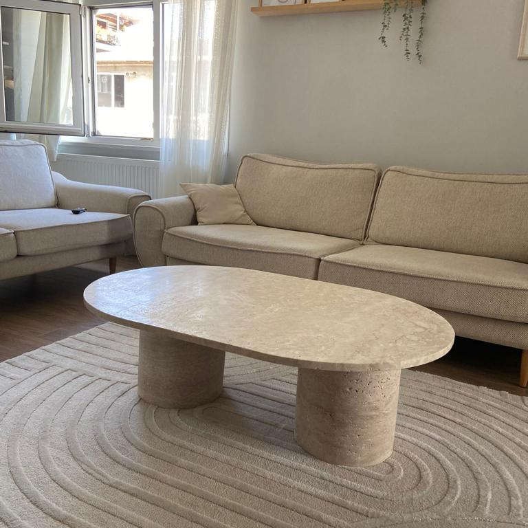 Interior of living room with Luzione travertine coffee table, beige sofa, and armchair, showcasing modern furniture and minimalist design