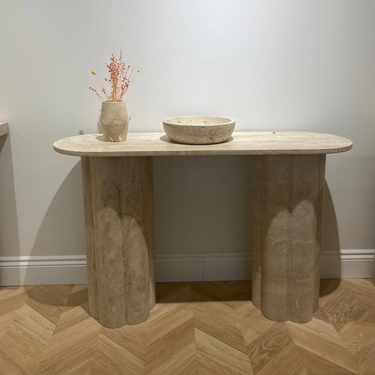 Travertine console table with fluted legs, vase, and bowl on wood floor
