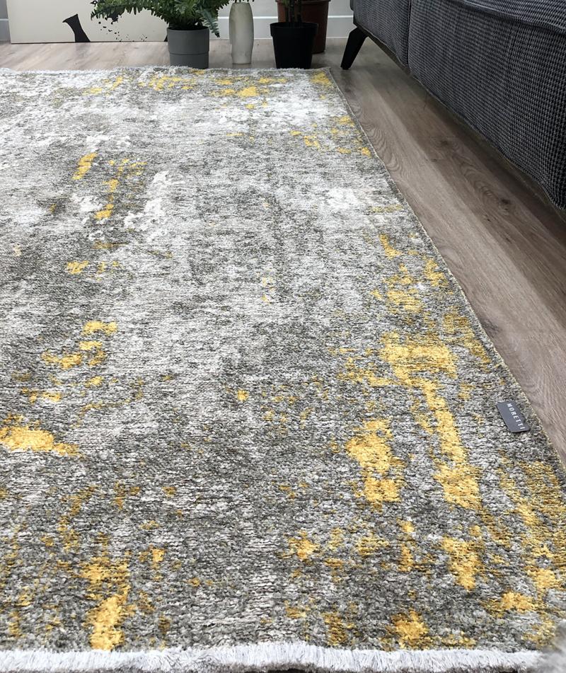 Close up view of gray and yellow abstract patterned rug on wood floor.