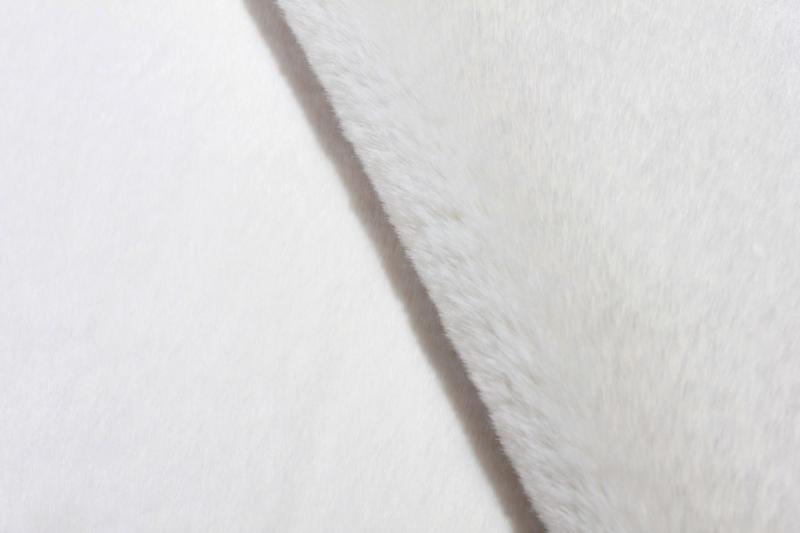 Angled view of cream sheep-textured rabbit fur rug under a coffee table, showcasing its soft texture.