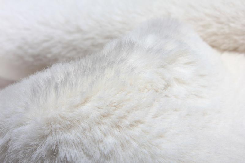 Angled view of cream sheep-textured rabbit fur rug under a coffee table, showcasing its soft texture.