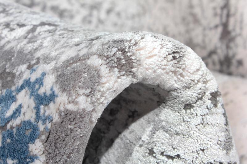 Close-up of folded Luzione 857 area rug showing blue, gray, and white abstract design and plush texture for home decor