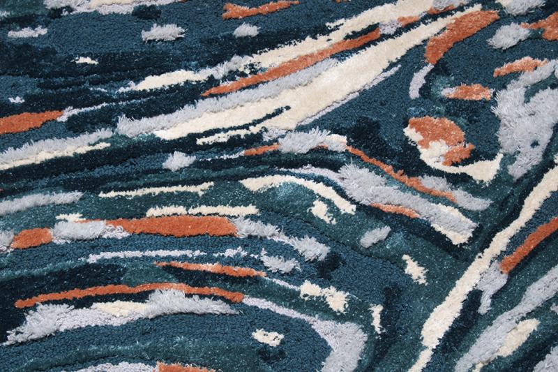 Close-up of the Luzione 902 Rock Tufted Rug featuring an abstract pattern with blue, orange, grey, and white colors. Soft shag texture for home decor