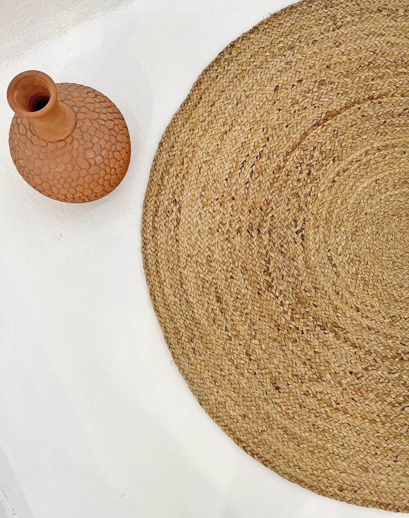 Overhead view terracotta vase next to round jute rug