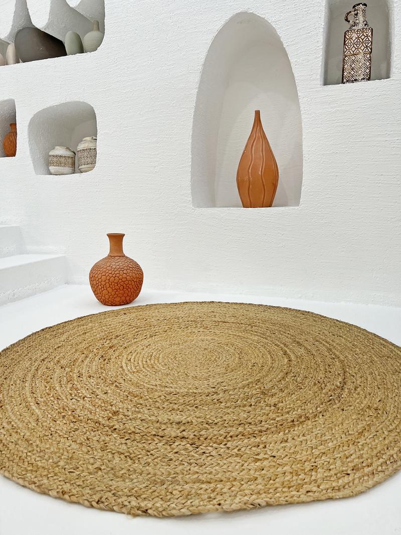 View of round natural fiber rug with terracotta vases on white floor and niches