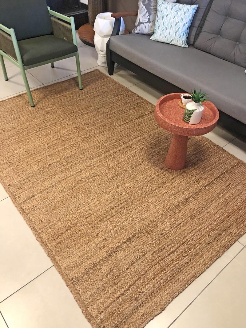 High-angle view of a living room featuring a Luzione jute rug, coral accent table, gray sofa, and green chair, creating a cozy and stylish space