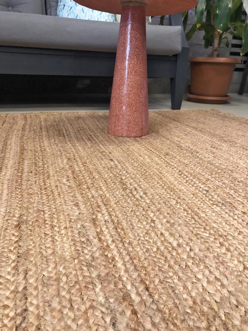 Close-up of Luzione 908 Urban Rug, a natural jute rug with textured weave, paired with a modern terracotta side table and gray outdoor sofa
