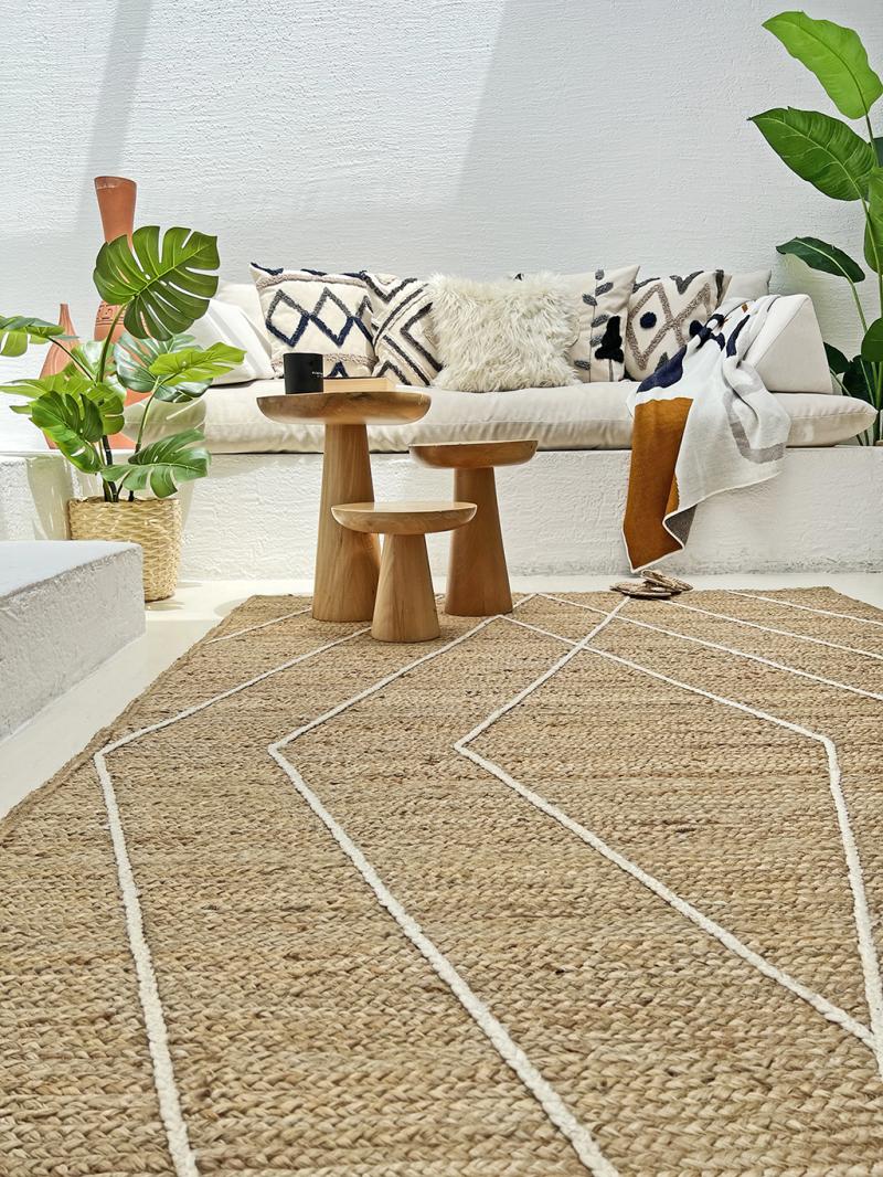 View of natural fiber rug with white geometric pattern in living space with wooden tables and sofa