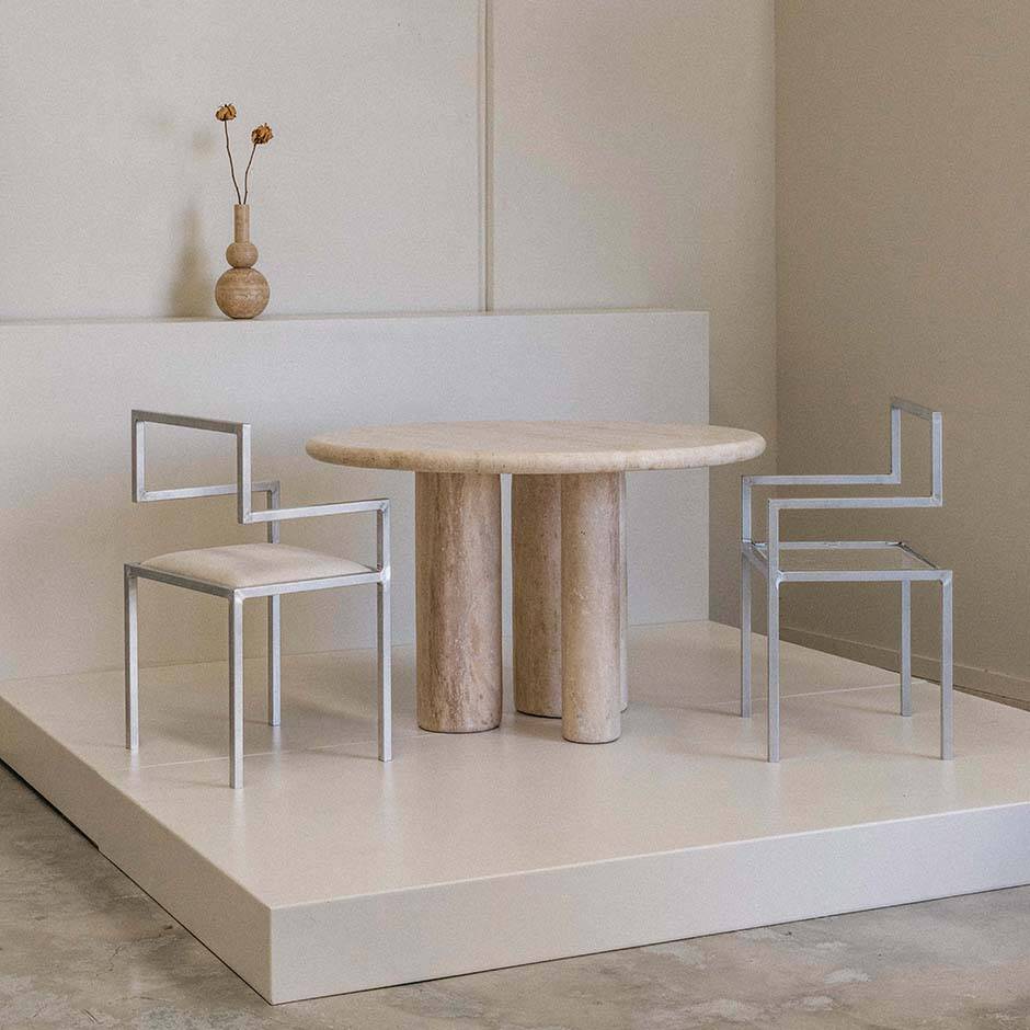 Luzione Karma Round Dining Table with travertine top and metal frame chairs showcasing modern minimalist interior design