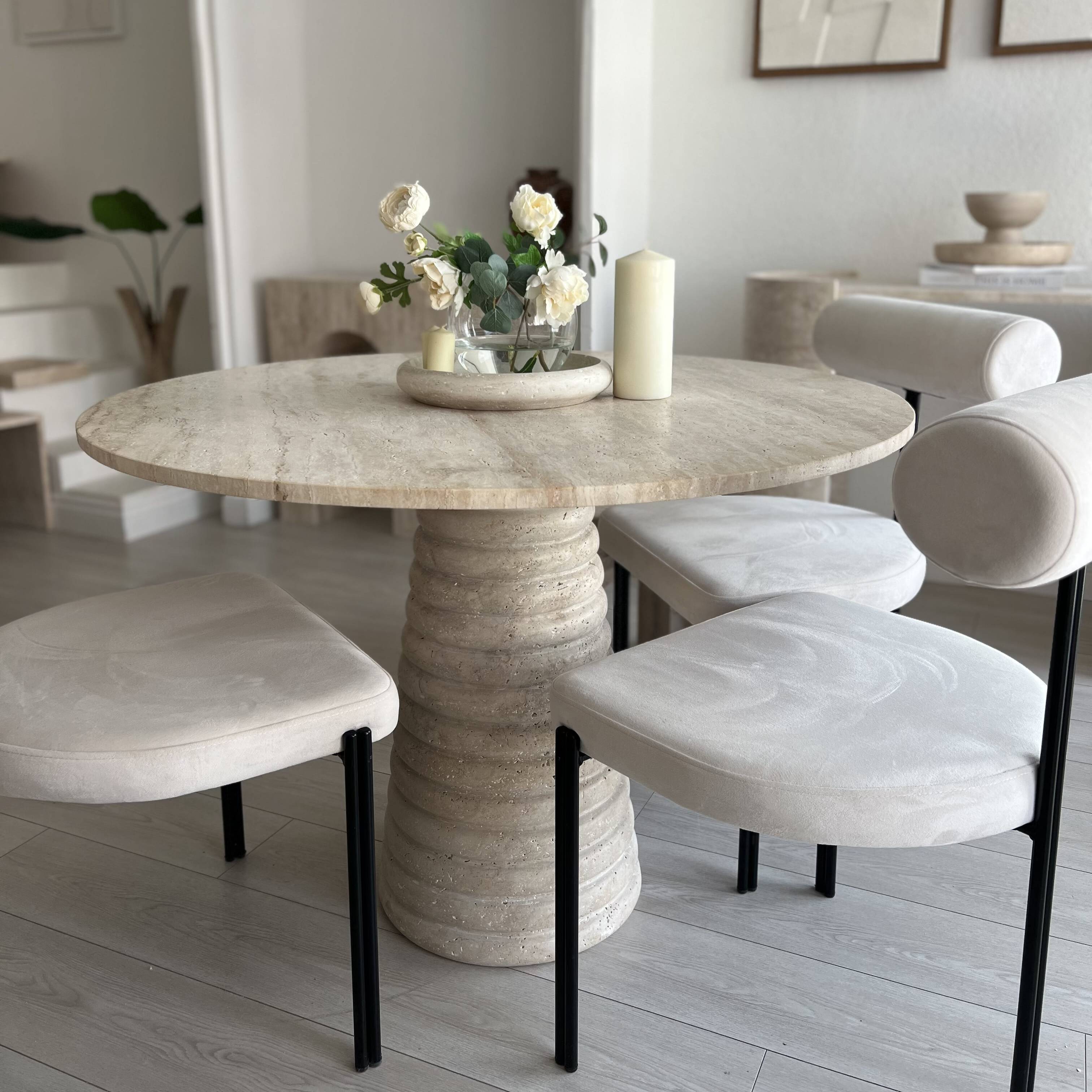 View of round travertine dining table with four upholstered chairs.