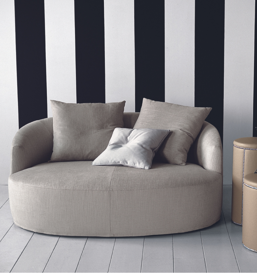 Interior view of Casamilano Francesca round sofa in beige with accent pillows against a striped wall, complemented by a side table