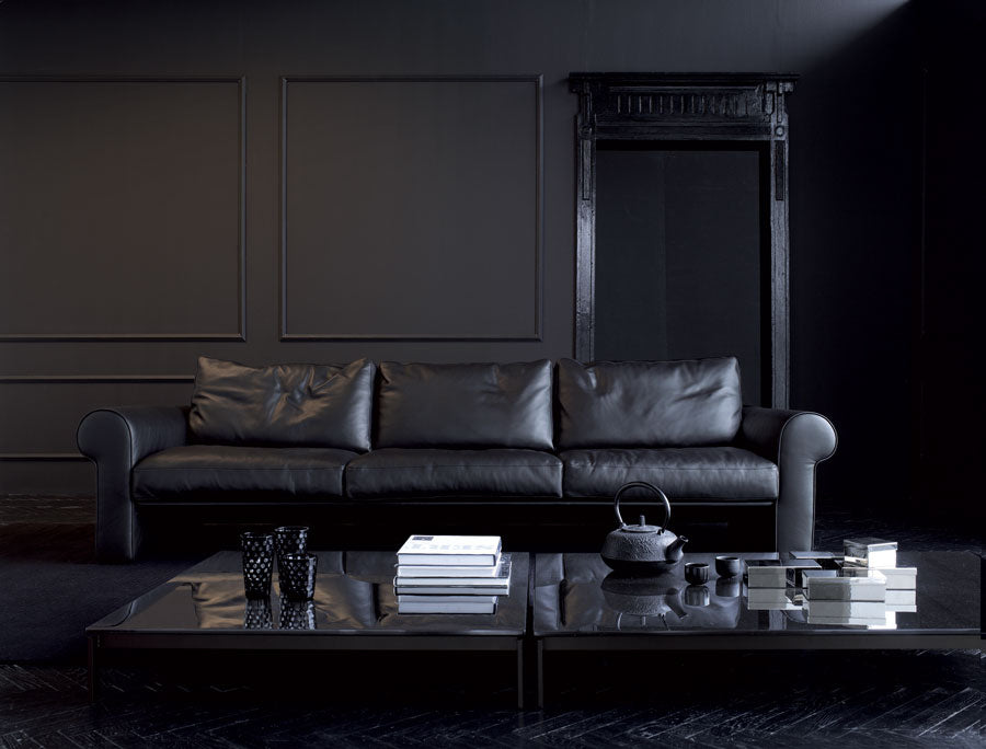 Black leather sofa and glass coffee table in dark room.