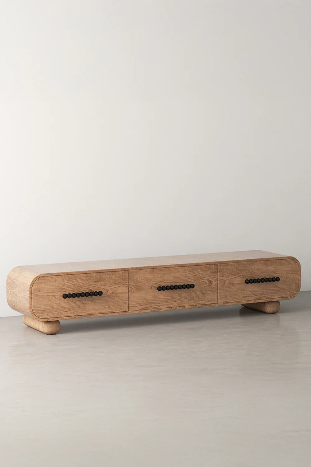 Long light wood media console with three drawers and black pulls.
