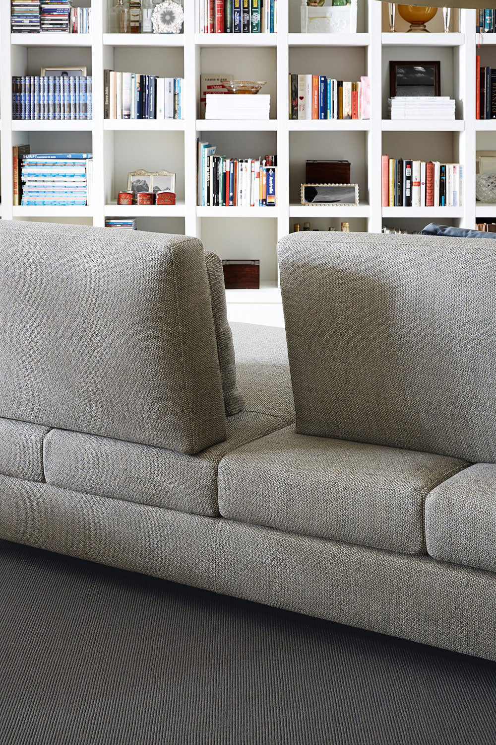 View of gray sectional sofa backrest against white built-in bookcase