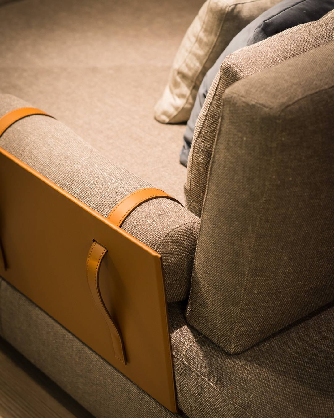 Close up of sofa armrest with tan leather panel and straps