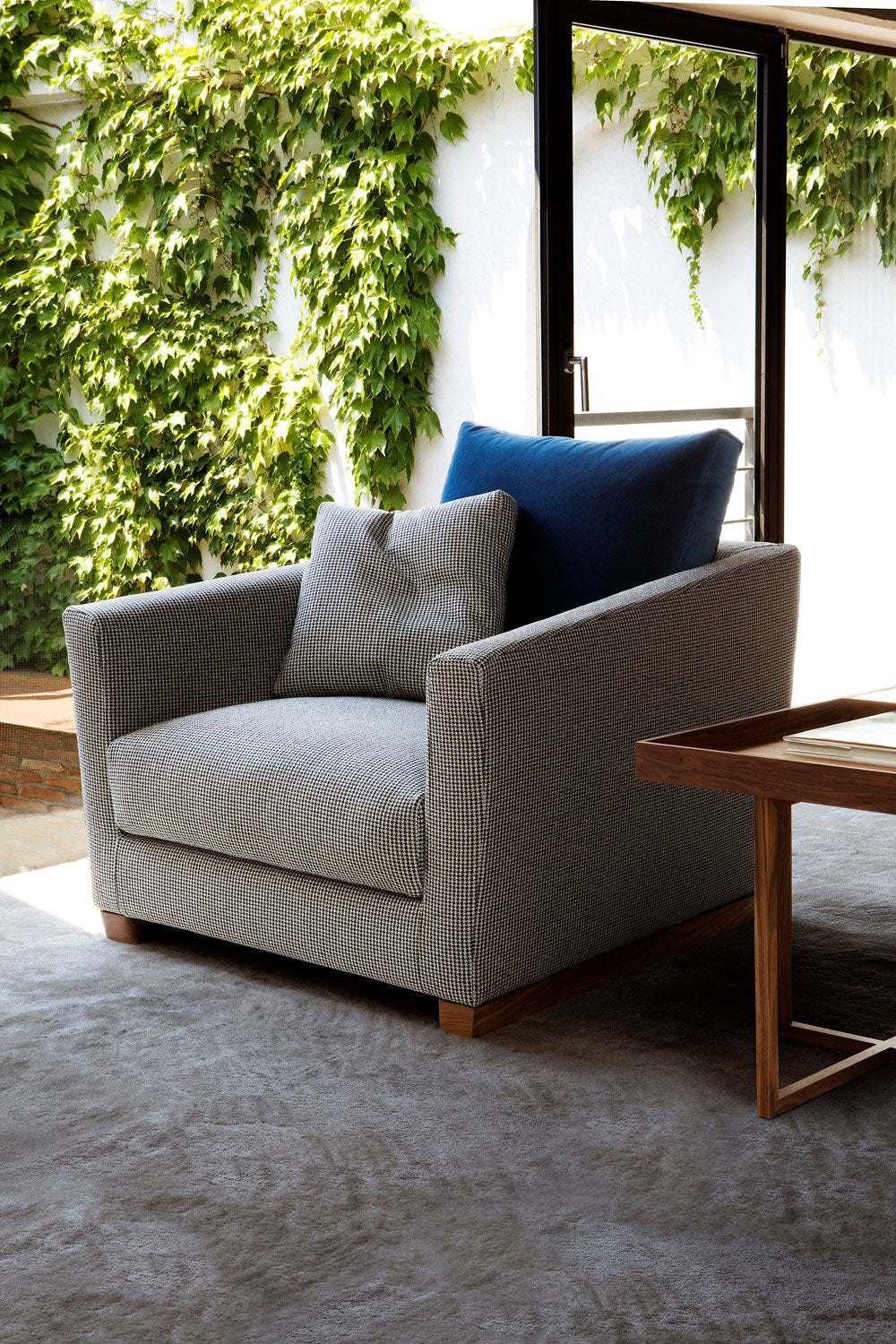 View of gray patterned armchair with blue cushion next to wooden table.