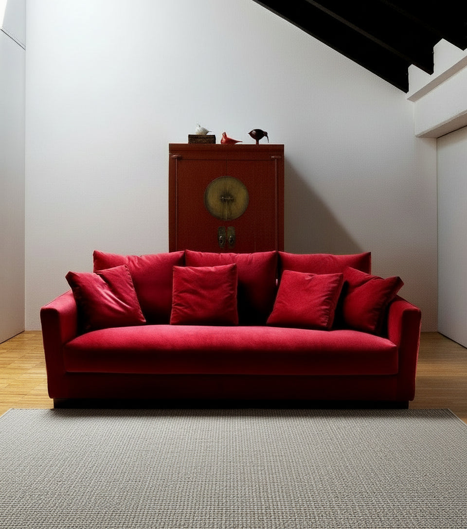 Attic living room with red velvet sofa, side table, red cabinet, gray rug, wood beams.