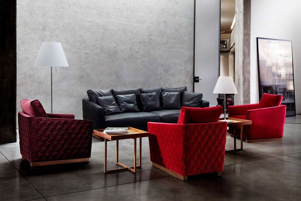 Industrial style living room with black leather sofa, red velvet armchairs, side tables, floor lamp.