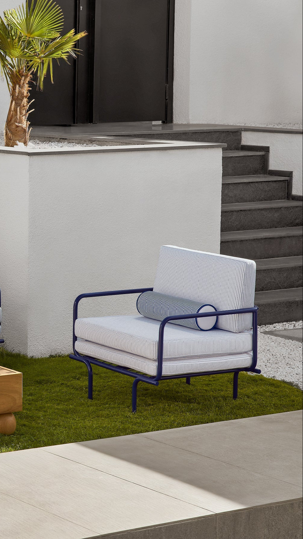 Modern outdoor chair with white cushions and blue metal frame on a grassy area.